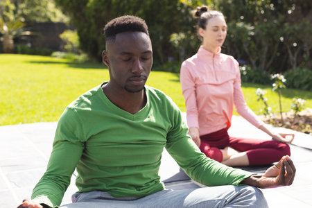 Diverse couple practicing yoga and meditating in garden. Lifestyle, togetherness, relationship, relaxation and domestic life, unaltered.の写真素材