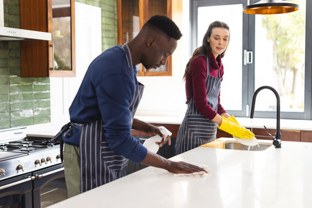 Happy diverse couple cleaning countertop and doing dishes in kitchen at home. Lifestyle,...