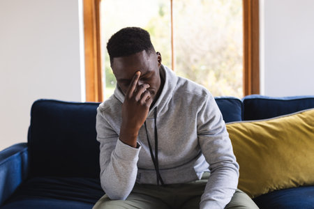 Sad african american man sitting on sofa having video call at home. Lifestyle, communication, video call and domestic life, unaltered.の写真素材