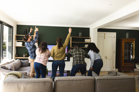 Excited diverse male and female friends watching sport on tv at home. Lifestyle, sport, competition, entertainment, friendship and domestic life, unaltered.の写真素材