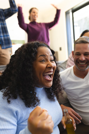 Excited diverse male and female friends watching sport on tv at home and drinking beers, copy space. Lifestyle, sport, competition, entertainment, friendship and domestic life, unaltered.の写真素材