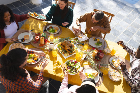 Happy diverse male and female friends eating thanksgiving celebration meal in sunny garden. Celebration, friendship, patriotism, american culture and tradition, unaltered.の写真素材