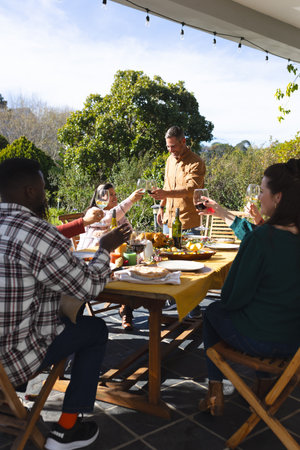 Happy diverse male and female friends toasting during thanksgiving celebration meal in sunny garden....