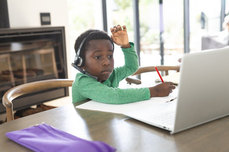 African american boy having online class using headphones and laptop with copy space, slow motion....