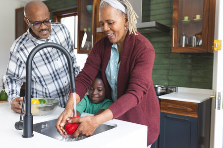 Happy african american grandparents and grandson washing vegetables in kitchen, slow motion. Food, cooking, home, family, togetherness, domestic life and lifestyle, unaltered.の写真素材