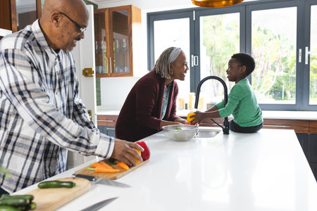 Happy african american grandmother and grandson washing vegetables in kitchen, slow motion. Food, cooking, home, family, togetherness, domestic life and lifestyle, unaltered.の写真素材