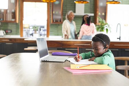 African american boy having online class using headphones and laptop with copy space, slow motion. Childhood, school, education, online learning, communication, domestic life and lifestyle, unaltered.の写真素材