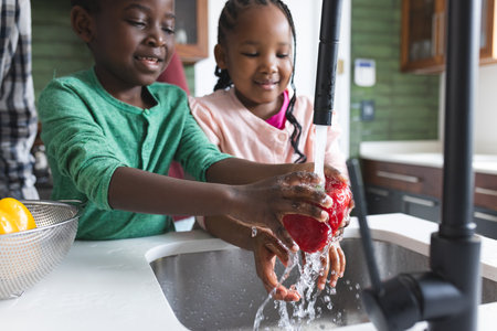 Happy african american grandfather and grandchildren washing vegetables in kitchen, slow motion. Food, cooking, home, family, togetherness, domestic life and lifestyle, unaltered.の写真素材