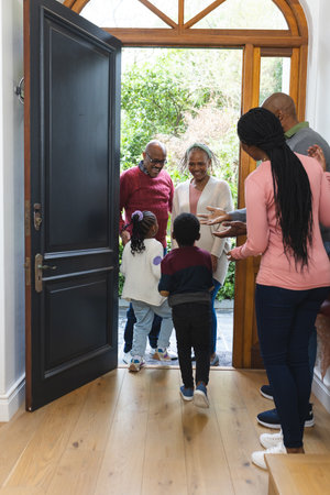 Happy african american parents, son and daughter welcoming grandparents at front door. Home, family,...