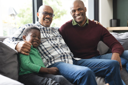 Happy african american father, son and grandfather sitting on couch,laughing and embracing....