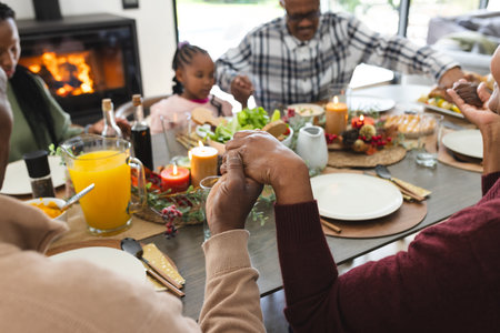 Happy african american multi generation family holding hands at thanksgiving dinner. Thanksgiving, celebration, meal, home, family, togetherness,の写真素材