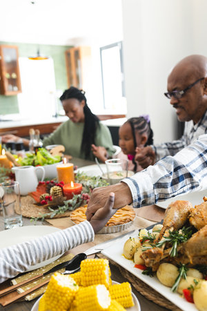 Happy african american multi generation family holding hands at thanksgiving dinner. Thanksgiving, celebration, meal, home, family, togetherness,の写真素材