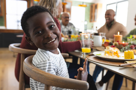 Portrait of african american son with family smiling at thanksgiving dinner table. Thanksgiving, celebration, tradition, meal, home, family, togetherness and lifestyle, unaltered.の写真素材