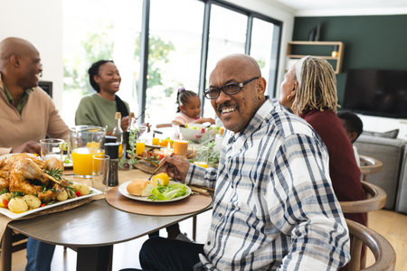Portrait of african american grandfather with family at thanksgiving dinner table. Thanksgiving, celebration, tradition, meal, home, family, togetherness and lifestyle, unaltered.の写真素材
