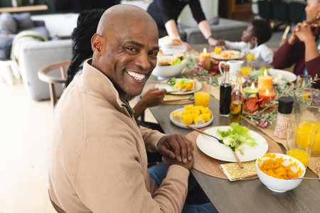 Portrait of african american father with family smiling at thanksgiving dinner table. Thanksgiving, celebration, tradition, meal, home, family, togetherness and lifestyle, unaltered.の写真素材