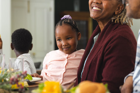 African american granddaughter sitting on grandmother's lap at thanksgiving dinner. Thanksgiving, celebration, meal, home, family, togetherness, unaltered.の写真素材