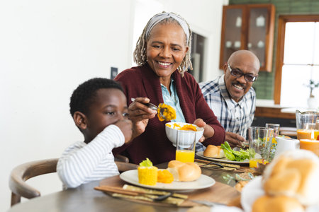 Happy african american grandmother serving food for grandson at thanksgiving dinner. Thanksgiving, celebration, meal, home, family, togetherness,の写真素材