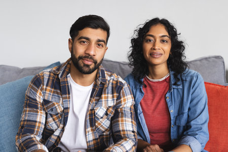 Happy biracial couple sitting on sofa and having video call in living room at home. Relationship, togetherness, lifestyle, free time and domestic life, communication, unaltered.の写真素材