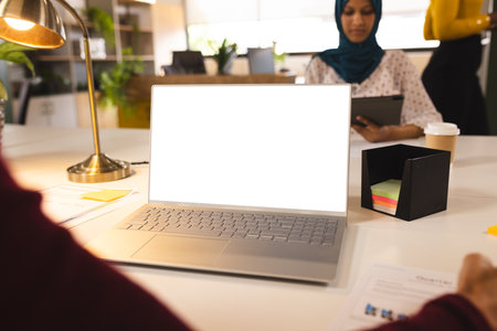 Caucasian casual businesswoman using laptop with copy space with colleagues in creative office. Business, technology and work, unaltered.の写真素材