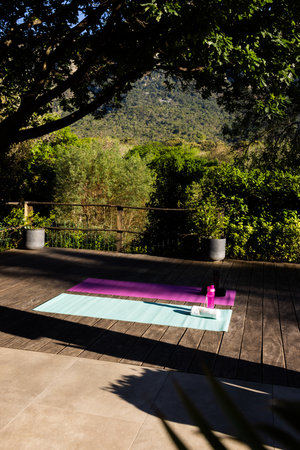 Water bottle, towel and two yoga mats side by side on deck in sunny garden, copy space. Yoga, nature, relaxation, fitness and heathy lifestyle.の写真素材