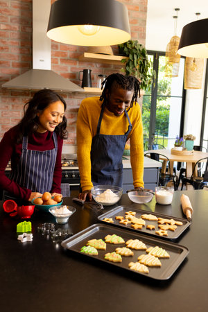 Happy diverse couple admiring freshly baked christmas cookies in kitchen, copy space. Cooking,...