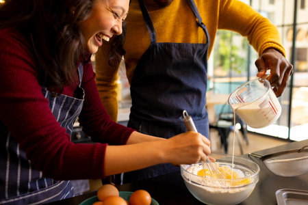 Happy diverse couple baking christmas cookies mixing dough in kitchen. Cooking, baking, food, christmas, celebration, tradition, togetherness, domestic life and lifestyle, unaltered.の写真素材