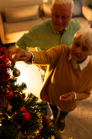 Happy caucasian senior couple decorating christmas tree in living room at home. Retirement, christmas, celebration, tradition,domestic life and senior lifestyle, unaltered.の写真素材