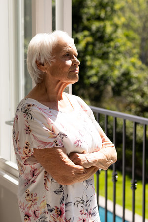 Pensive caucasian senior woman standing and looking ahead on balcony on sunny day. Retirement, domestic life and senior lifestyle, unaltered.の写真素材