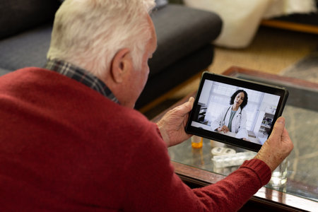 Caucasian senior man having video call with doctor in sunny living room. Retirement, health and...