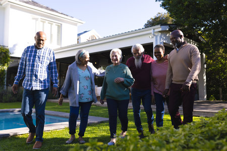 Happy diverse group of senior friends walking next to pool in sunny garden. Retirement, friendship, wellbeing, togetherness and senior lifestyle, unaltered.の写真素材