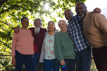 Happy diverse group of senior friends embracing and smiling in sunny garden. Retirement, friendship, wellbeing, nature, togetherness and senior lifestyle, unaltered.の写真素材