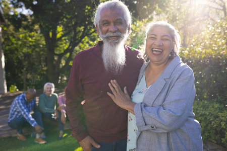 Happy biracial couple of senior friends embracing and smiling in sunny garden. Retirement,...