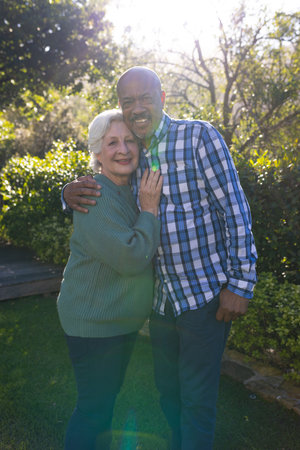Happy diverse couple of senior friends embracing and smiling in sunny garden. Retirement, friendship, wellbeing, togetherness and senior lifestyle, unaltered.の写真素材