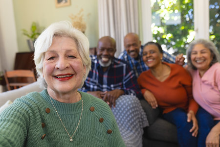 Happy caucasian senior woman doing selfie and smiling in sunny living room, copy space. Retirement, domestic life and senior lifestyle, communication, technology, unaltered.の写真素材