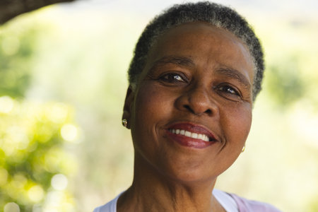 Head of happy african american senior woman smiling in sunny garden, copy space. Retirement, wellbeing and senior lifestyle, unaltered.の写真素材