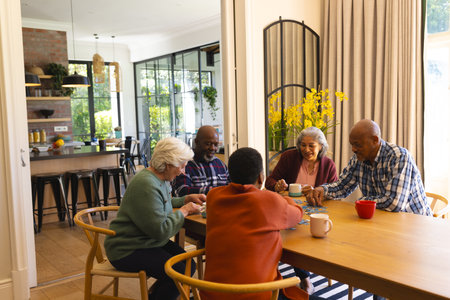 Happy diverse group of senior friends playing with jigsaw puzzles in sunny dining room at home. Retirement, friendship, wellbeing, activities, togetherness and senior lifestyle, unaltered.の写真素材