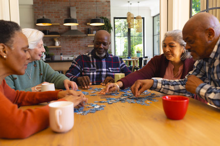 Happy diverse group of senior friends playing with jigsaw puzzles in sunny dining room at home....
