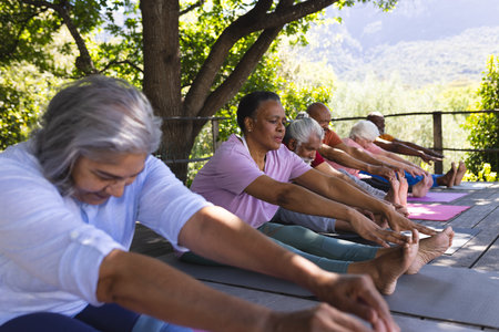 Happy diverse group of senior friends stretching at yoga class in sunny garden, copy space. Retirement, friendship, wellbeing, yoga, fitness and healthy senior lifestyle, unaltered.の写真素材