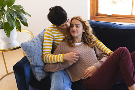 Happy biracial lesbian couple relaxing on couch together embracing at home. Gay, love, relationship,...