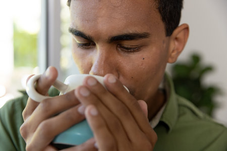 Biracial man drinking coffee and standing next to window at home. Lifestyle and domestic life, unaltered.の写真素材