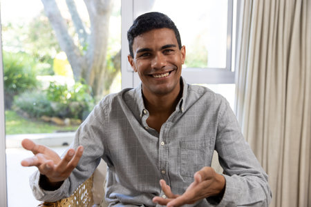 Happy biracial man sitting on armchair having video call at home. Communication, lifestyle and...