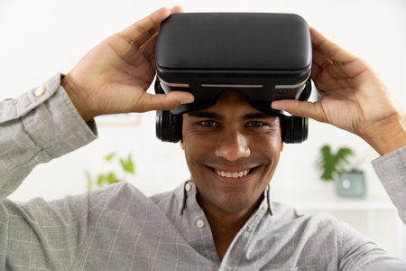 Portrait of happy biracial man using vr headset at home. Technology, communication, lifestyle and...