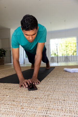 Biracial man exercising and using smartphone at home. Fitness, communication, active lifestyle and...