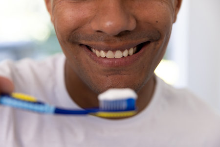Happy biracial man holding toothbrush in bathroom at home. Self care, hygiene, lifestyle and domestic life, unaltered.の写真素材