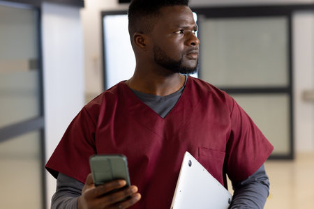 African american male doctor using smartphone in hospital corridor. Medicine, healthcare,...
