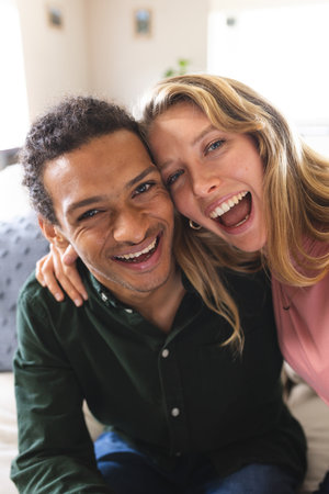 Happy diverse couple having video call and laughing in sunny living room. Lifestyle, free time and...