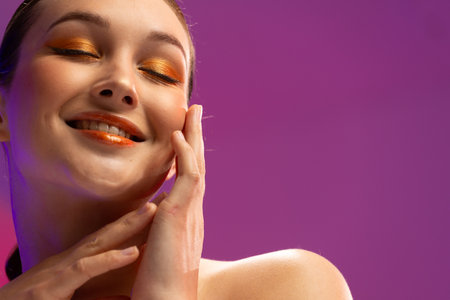 Caucasian woman wearing orange eye shadow and lip gloss on purple background, copy space. Cosmetics,...