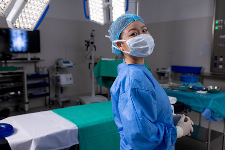 Portrait of asian female doctor with face mask and gloves in hospital operating room. Medicine, healthcare and medical services, unaltered.の写真素材