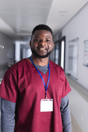 Portrait of happy african american male doctor in hospital corridor. Medicine, healthcare and medical services, unaltered.の写真素材