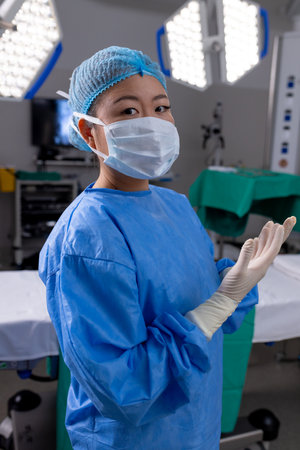 Portrait of asian female doctor with face mask and gloves in hospital operating room. Medicine, healthcare and medical services, unaltered.の写真素材